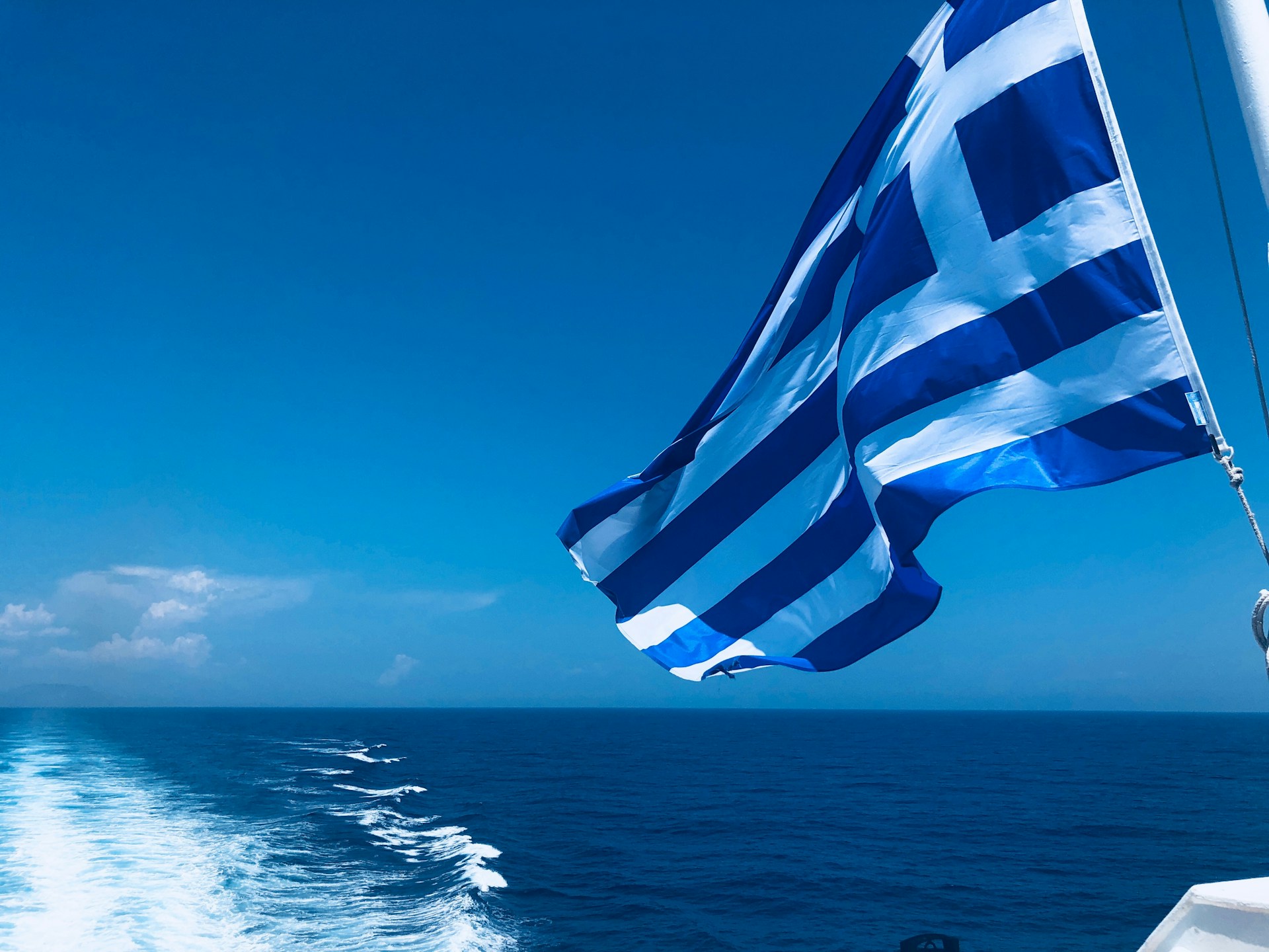 Greek flag on the sea; image by Lisa Boonaerts on unsplash